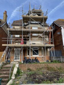 Scaffolding across the front of a Folkestone property, with render removed to expose the brickwork before wall tie replacement.